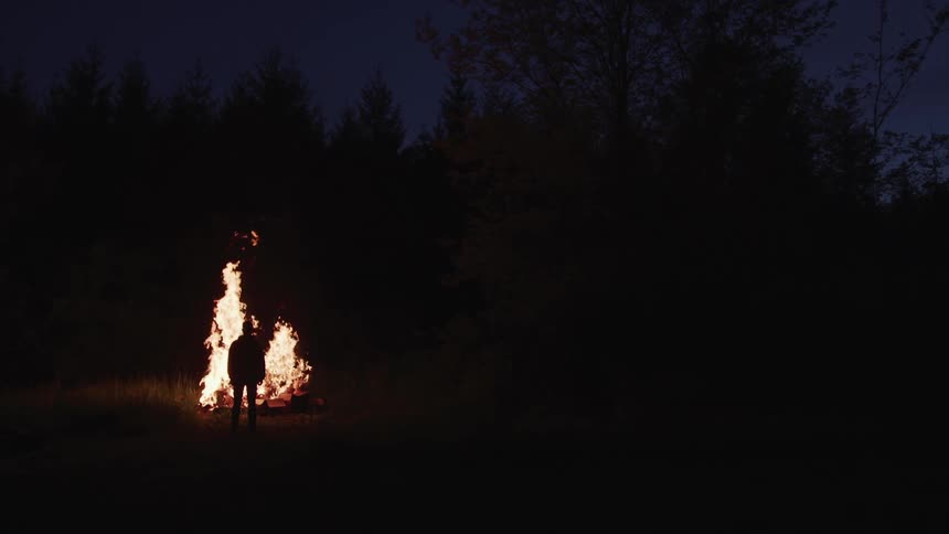 Person standing near bonfire is cast into silhouette at night