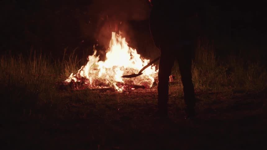 A person shovels dirt by an openly burning brush fire