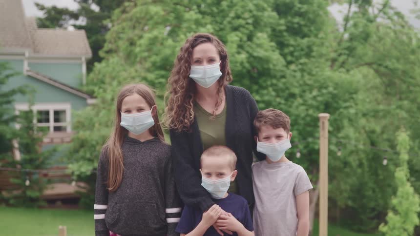 Mother sons and daughter wearing face masks stand and pose for the camera in the garden