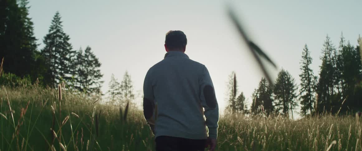 A man walks through a field with waist high grass