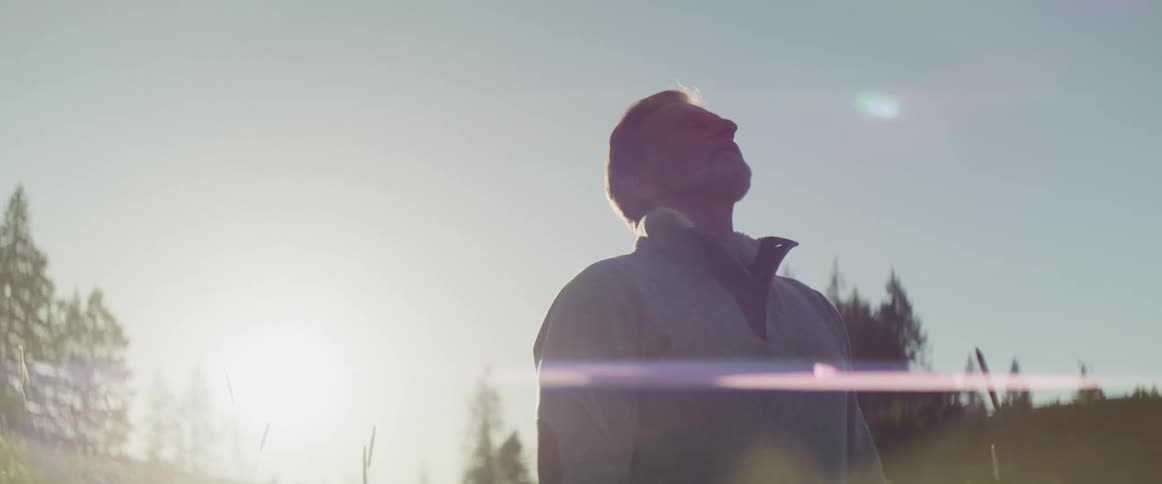 A man in a sweater stands outside on a sunny day