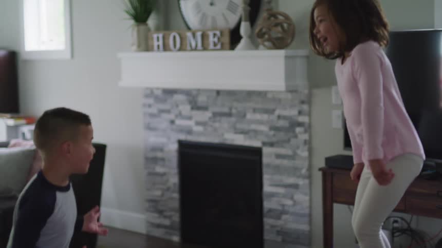 Children with grey and pink long sleeve t shirt jump on a sofa in the living room