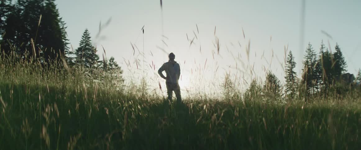 A person standing in a grassy field with trees the sky and clouds in the background