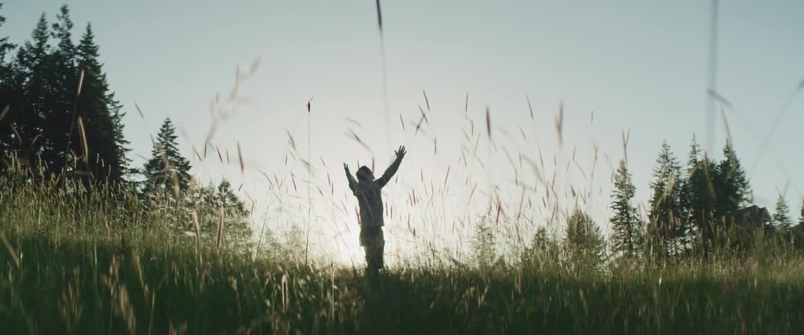 A man stands in a grassy field with his arms raised up into the sky above his head