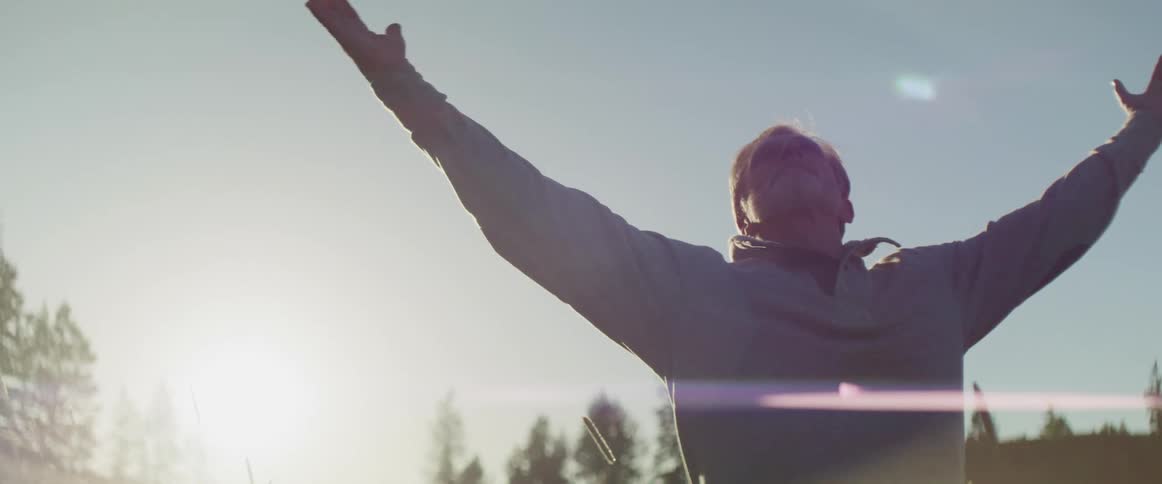 A man standing outside with the sun shining down on him raises his arms in to the air