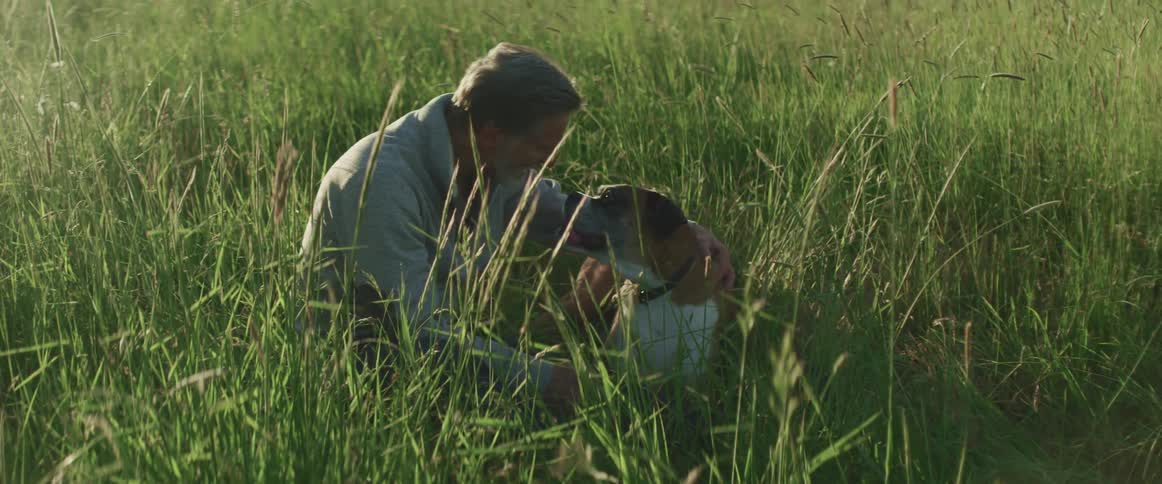 A man kneeling to pet his dog while in a field during the day