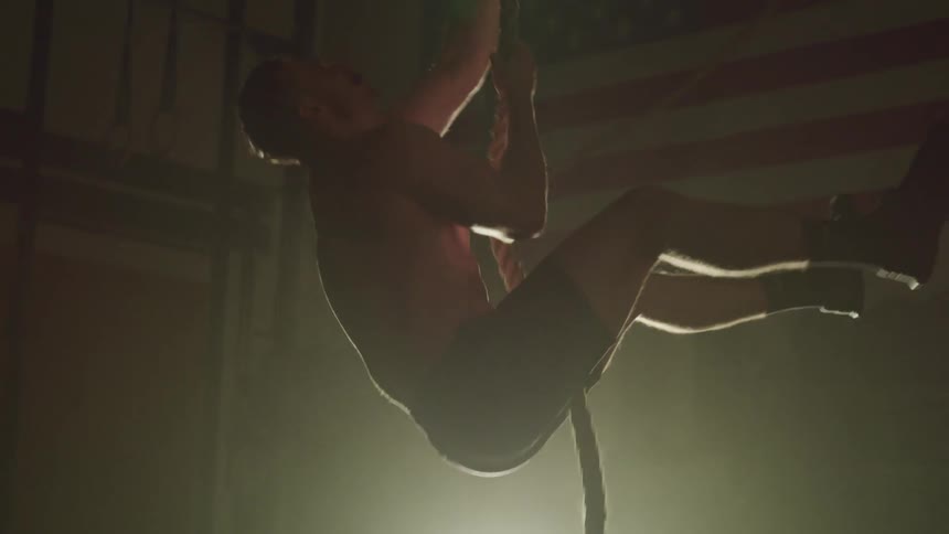 A man is working out and climbing a rope