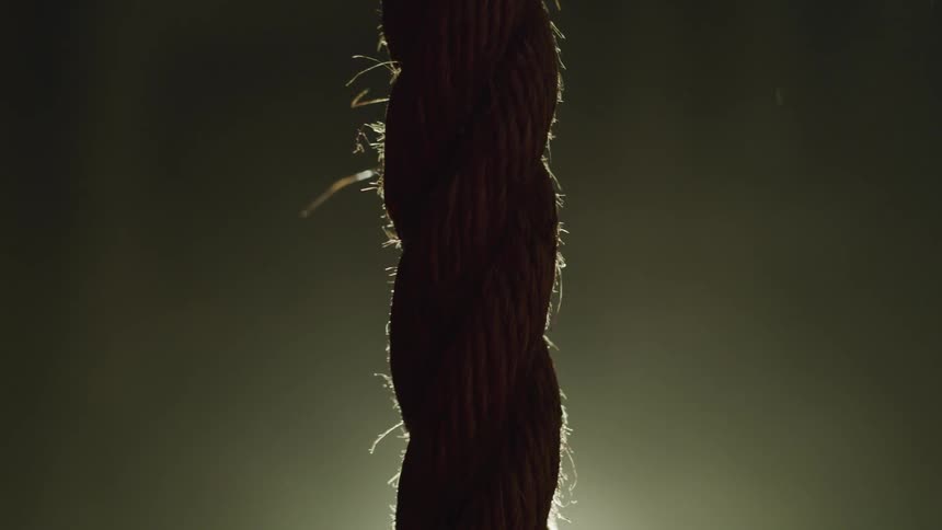A single piece of rope dangles in front a a bright light that reveals the ropes fibers