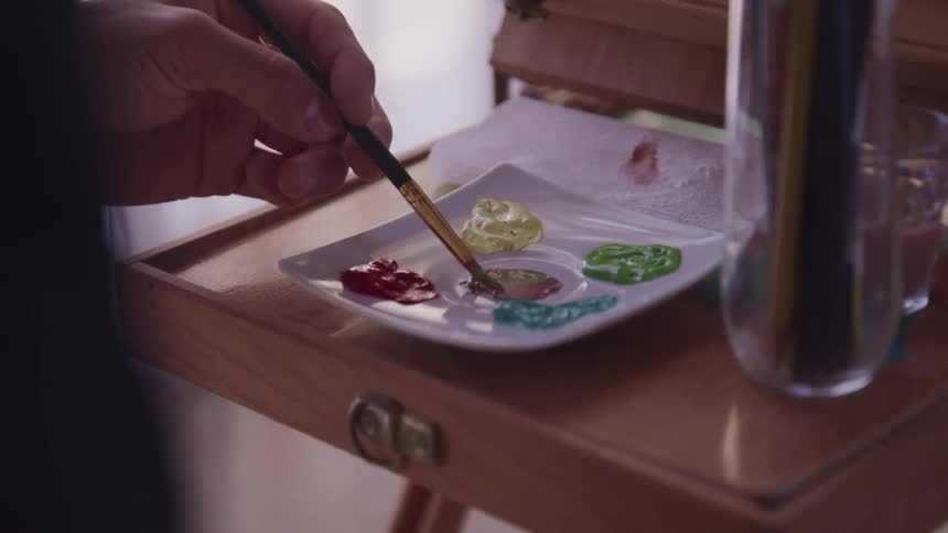 Paintbrush being dipped into a dab of paint on a dish