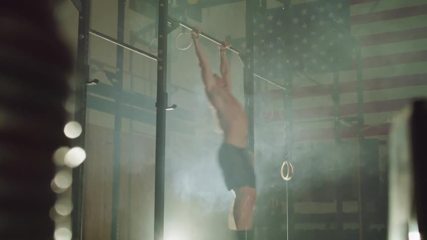 A male gymnast spins and lifts himself on a horizontal bar before jumping off