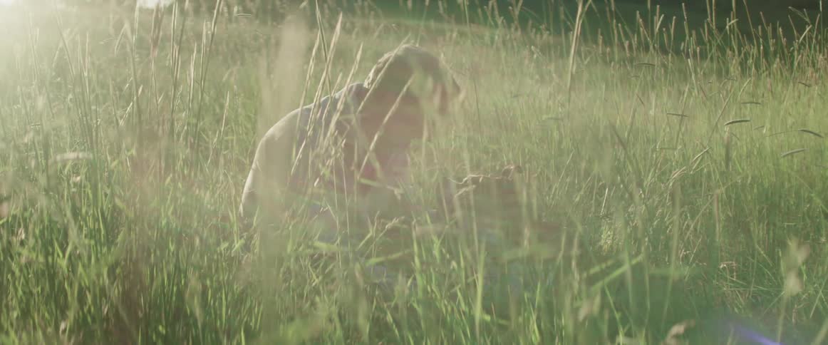 A man sits in a grassy field and pets his dog