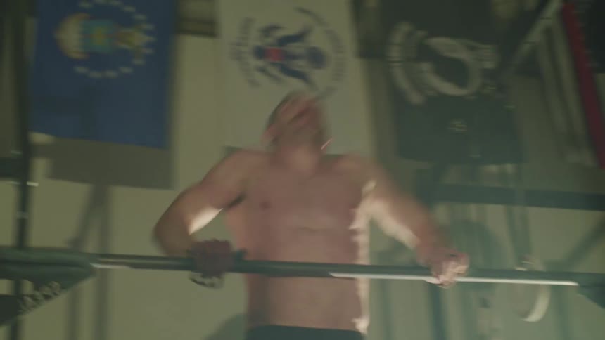 Muscular man grips a bar and does pull ups in a gym