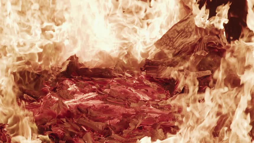 A raging fire burns furiously as it engulfs and consumes a pile of paper