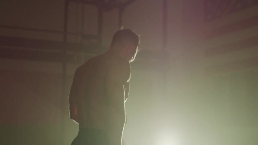 Bare chested man uses dumbbells standing in foggy room with american flag on the wall