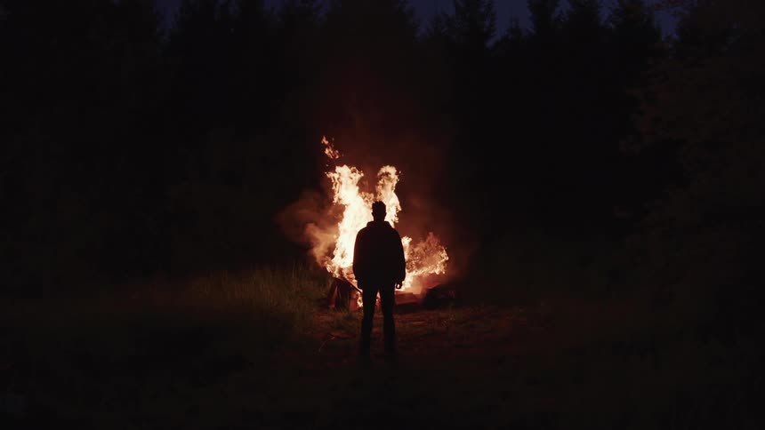A man is standing by a bonfire at night