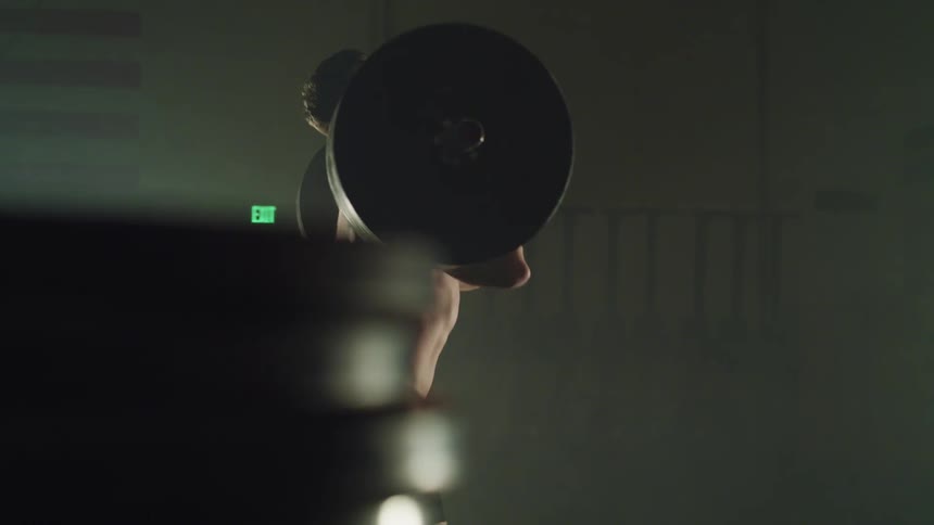 Man lifts large heavy weight bar over his head in foggy room