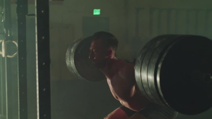A man lifts large weights in a dimly lit gym