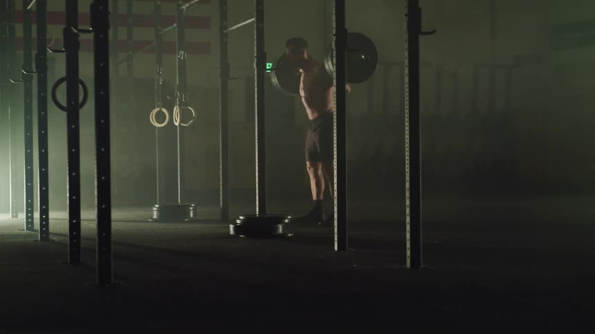 Muscular man squats with a barbell in a gym