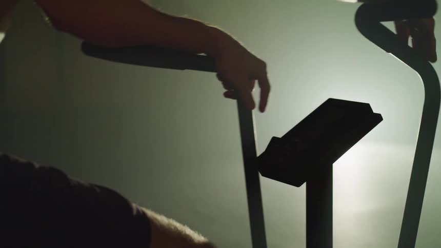 A man slowly rides an exercise bicycle as a bright light shines on him