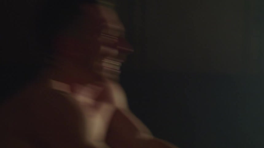 Bare chested man exercises on rowing machine in dim room