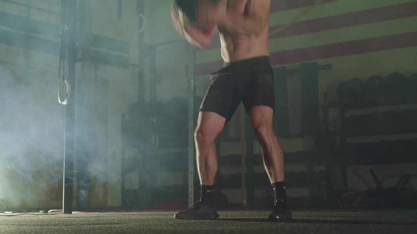 A man throws a medicine ball up and down in the gym