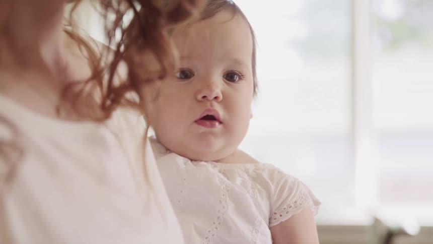 A woman holding a baby with a window in the background