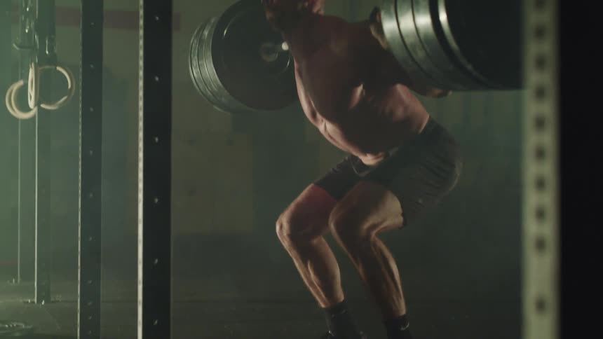 Muscular man squats with a barbell in a gym