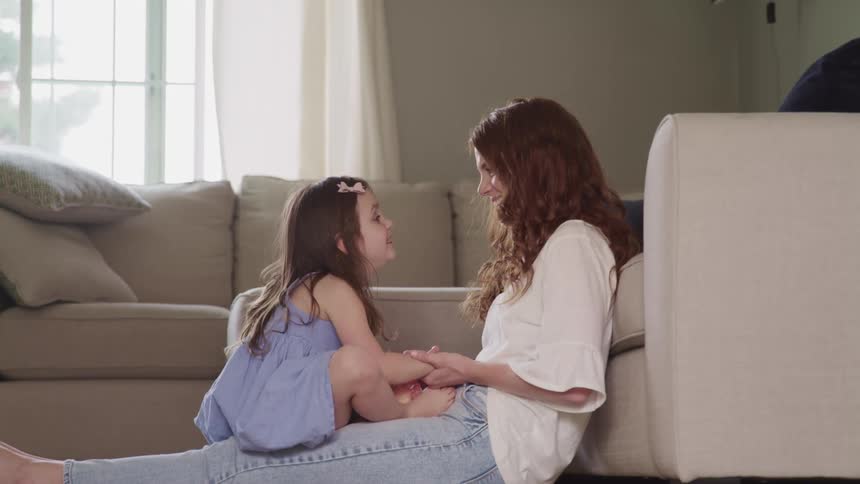 A woman sitting next to a couch with a little girl sitting on her lap facing her and talking