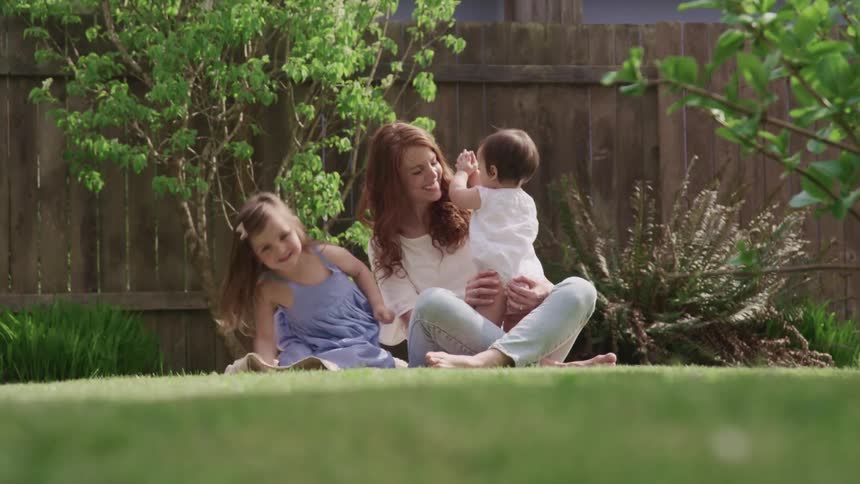 Mother playing with her children while sitting on the grass in the backyard