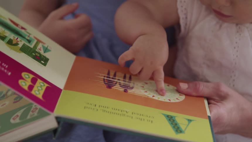 Mother holds two children on her lap as they look at a book