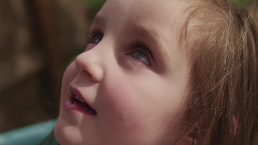 Little girl with brown hair looks up and smiles slightly