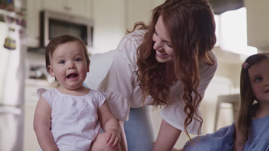 A young women stands near her baby and young child in the kitchen of her house