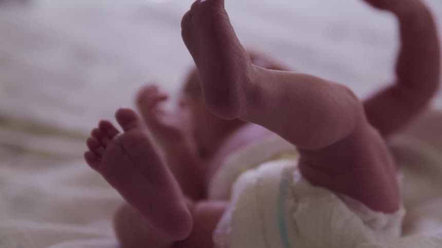 Baby lies on back on white spread kicking feet in air