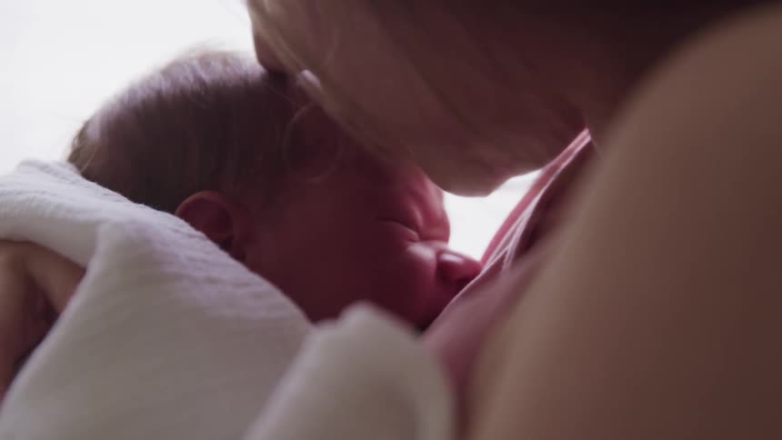 Woman with a pink short sleeve t shirt holds her baby and kisses its forehead