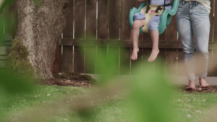 Daughter sits in swing located in the backyard as her mother pushes her