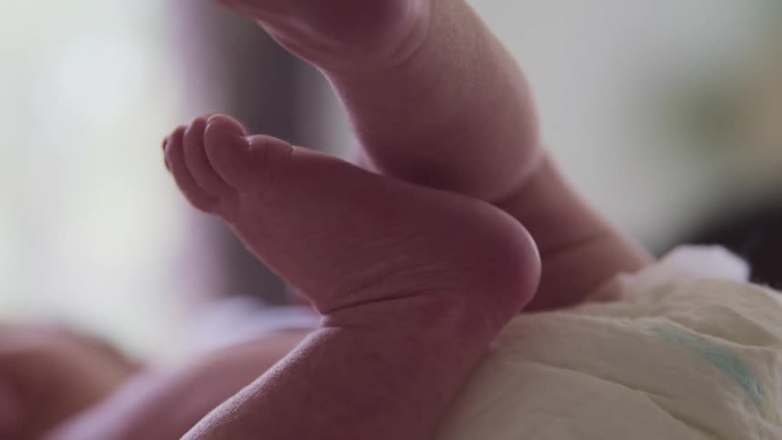 New born baby wearing a diaper lying down on her back and moves its feet