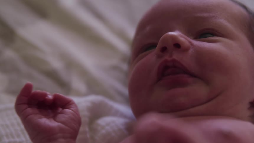 An infant rolls from its side to its back as it lies on a blanket