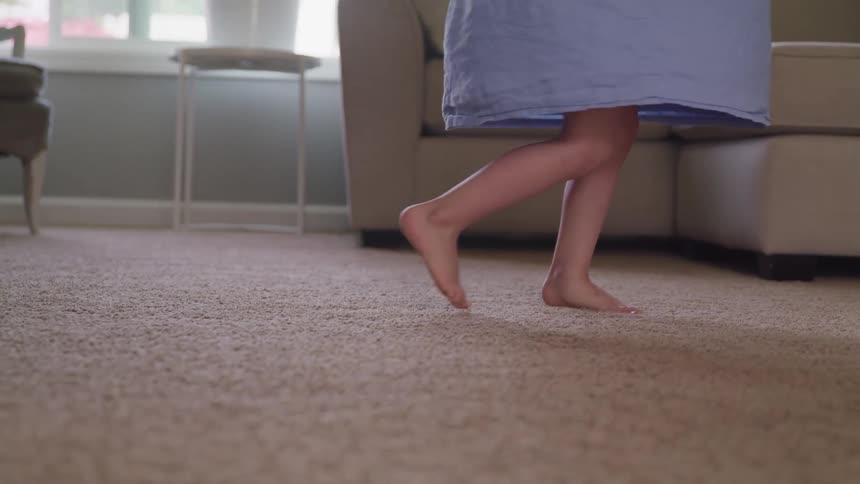 A barefoot toddler in a dress spins around in a living room