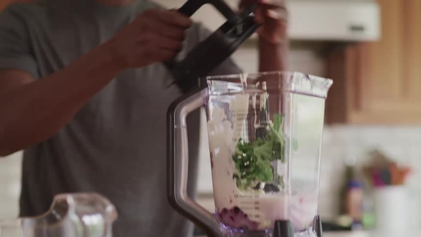 A man places a blender on its base and puts the lid on top in a home kitchen