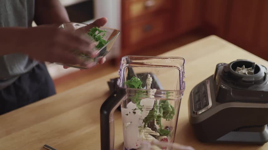 A man is placing vegetables and yogurt in a blender
