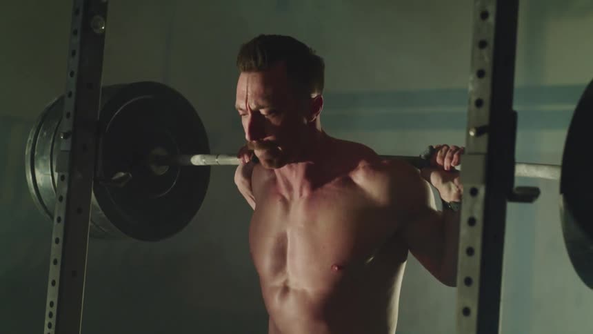A man does squats while holding a barbell equipped with large weights