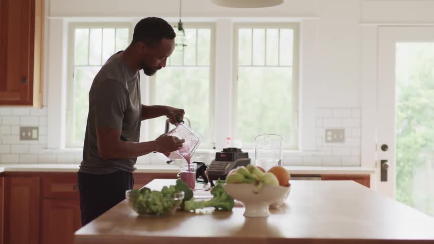 A man pours a smoothie from a blender into a glass