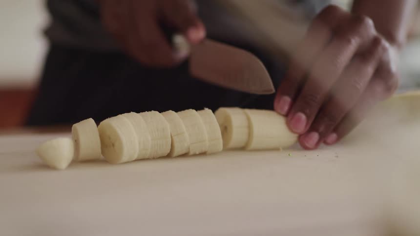 Black man cuts a banana with a knife in the kitchen