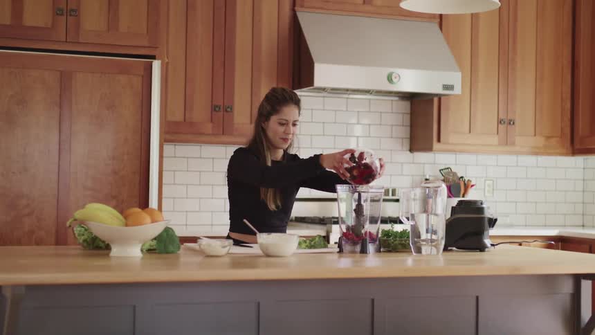 A woman pours berries from a glass bowl into a blender