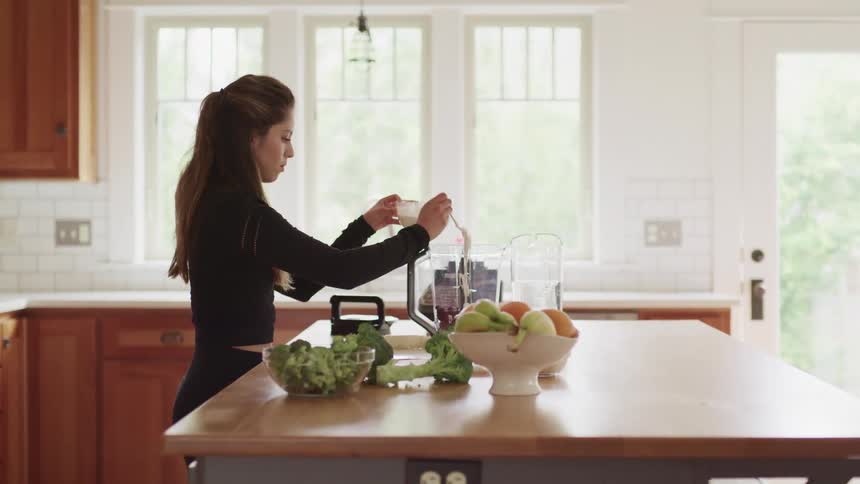 Woman adds ingredients to blender sitting on kitchen island