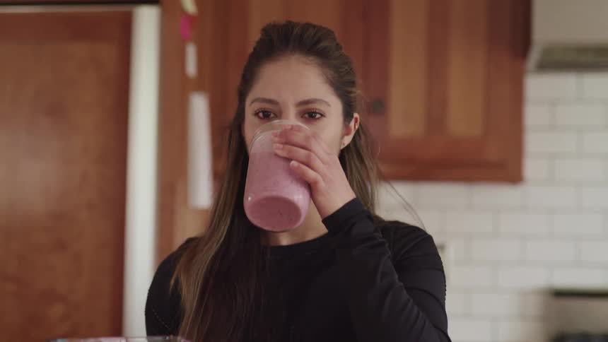 A woman drinks a smoothie in the kitchen