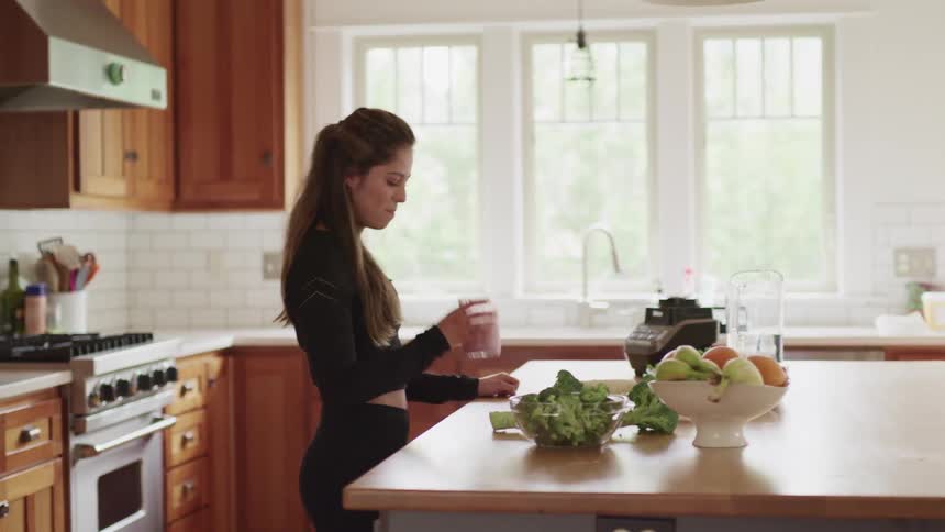 A woman stands in her kitchen drinking from a glass