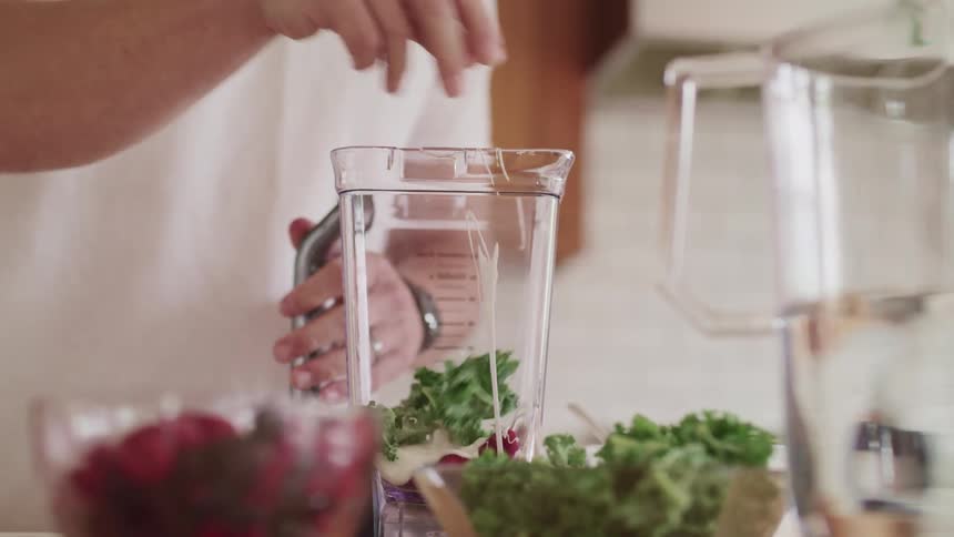 Man wearing white shirt puts vegetables inside a mixer vase to make juice in the kitchen at home