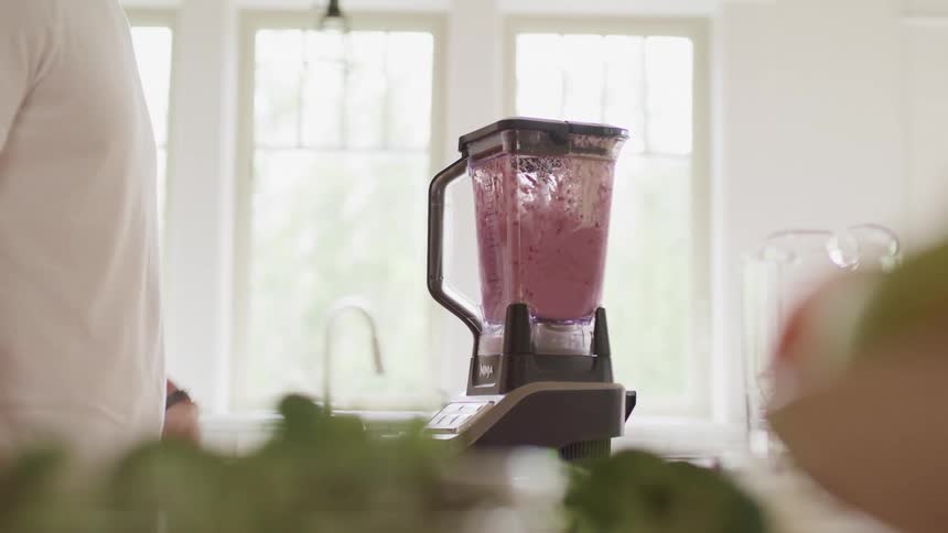 A man blends berries in a blender in the kitchen during the day