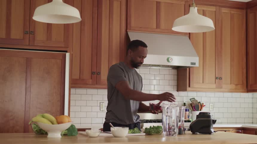 A man adds berries to a blender to make a smoothie